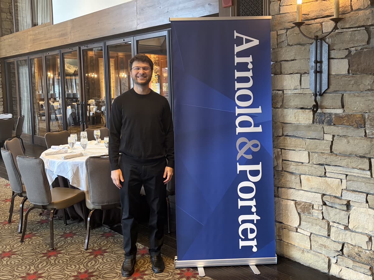 Leo standing beside an Arnold & Porter banner in Park City, Utah.
